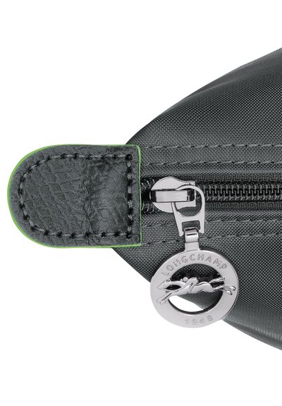 Graue Nylon-Tasche mit Reißverschluss und schwarzem Leder-Zipper, ausgestattet mit grünen Nähten und einem silbernen Anhänger mit "LONGCHAMP 1948" und Logo.