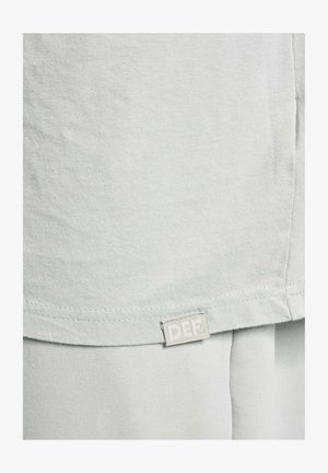 Világosszürke pamut póló, puha tapintással, az alsó szegélyen egy "DEF" felirattal ellátott kis címkével. Egyszerű, rövidujjú dizájn.