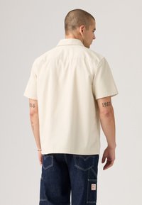 Short-sleeve beige shirt with a flat collar, a relaxed fit, and a smooth texture. Features short sleeves and a straight hemline.