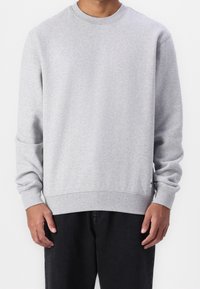 Sweat-shirt en coton gris à manches longues, col rond, poignets et ourlet côtelés. Comprend un petit patch logo sur le côté inférieur.