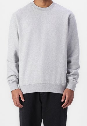 Sweat-shirt en coton gris à manches longues, col rond, poignets et ourlet côtelés. Comprend un petit patch logo sur le côté inférieur.