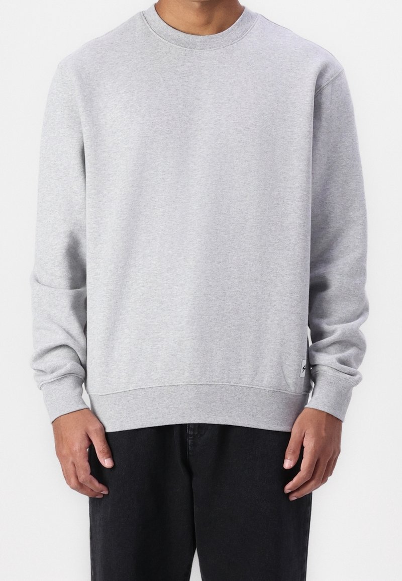 Sweat-shirt en coton gris à manches longues, col rond, poignets et ourlet côtelés. Comprend un petit patch logo sur le côté inférieur.