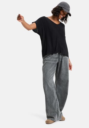 Black loose-fitting short-sleeve top with a V-neck, paired with high-waisted, wide-leg gray jeans and beige slip-on shoes.
