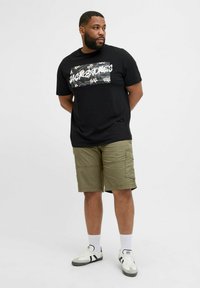 Black T-shirt with floral graphic, olive cargo shorts, and white socks with sneakers. Focus on relaxed fit and casual style.