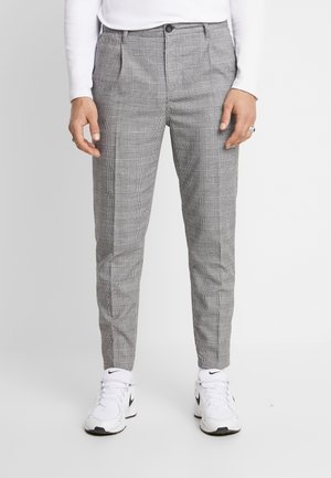 Schmal geschnittene graue Karohose, getragen mit weißen Nike-Sneakern und einem weißen Langarmshirt, von der Taille bis zu den Füßen abgebildet.