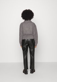 Grey knitted sweater with a high neck and ribbed texture, paired with black leather pants and chunky black shoes, viewed from the back.