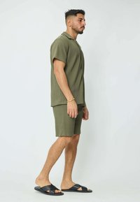 Chemise à manches courtes côtelée vert olive et short assorti, associés à des sandales à glissière noires. Design simple avec une coupe décontractée et un matériel minimal.