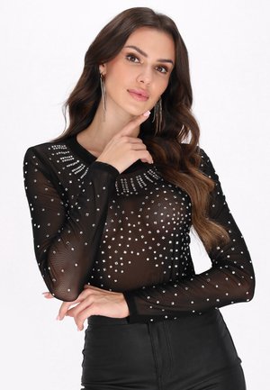 Černý síťovaný top s dlouhým rukávem zdobený stříbrnými rhinestones v geometrickém vzoru, s kulatým výstřihem a černými manžetovými rukávy.