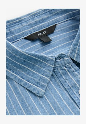 Modra denim srajca z belimi navpičnimi črtami, ki ima ovratnik s gumbi in oznako blagovne znamke "NEXT", ter prikazuje teksturirano tkanino.