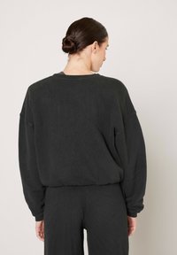 Dark gray oversized sweatshirt with a textured fabric, drop shoulder seams, and a relaxed fit. Features ribbed cuffs and hem.