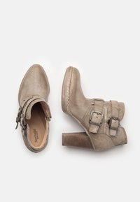 Botas de tobillo beige con un acabado texturizado, dos hebillas ajustables y un tacón de bloque. Detalles de costura alrededor de la suela.