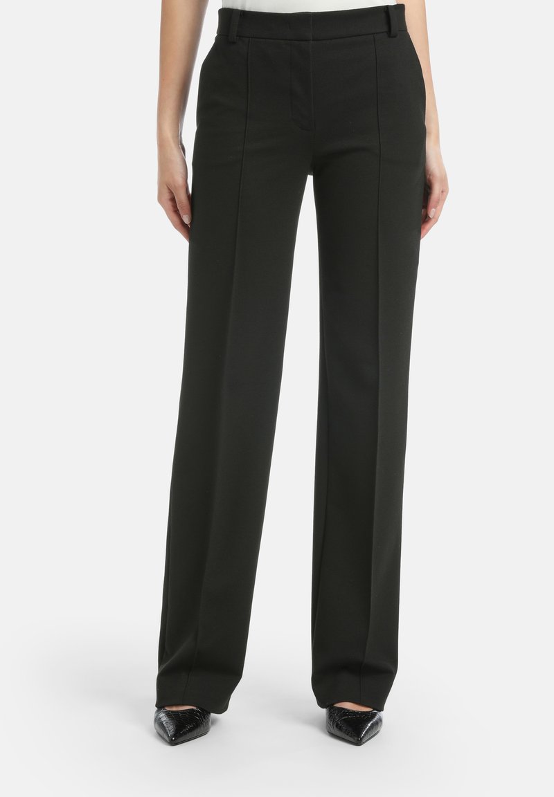 Zwarte, hoog geplaatst broek met een rechte pijp, met voorplooien en een gladde textuur. Draagt met zwarte schoenen met een spitse neus.
