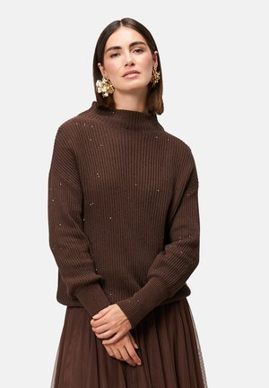 Bruine geribbelde trui met een hoge halslijn, voorzien van kleine decoratieve accenten op het oppervlak. Losse pasvorm en gebreide textuur.