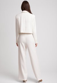 Biały krótki żakiet z długimi rękawami, gładką teksturą i klapami w język w połączeniu z dopasowanymi spodniami o szerokich nogawkach. Minimalistyczny design.