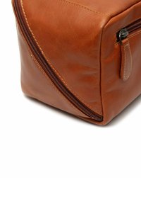 Neceser de cuero marrón con una textura suave, forma rectangular y un zipper lateral. Presenta un detalle de costura curvada en un lado.