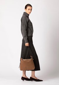 Suéter de cuello alto de punto gris combinado con una falda negra y fluida. La modelo lleva un bolso marrón de ante con acabado suave y correa de hombro negra.