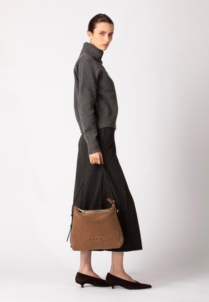 Grijze, gebreide coltrui gecombineerd met een zwarte, vloeiende rok. Model draagt een bruine suède tas met een gladde afwerking en een zwarte schouderriem.