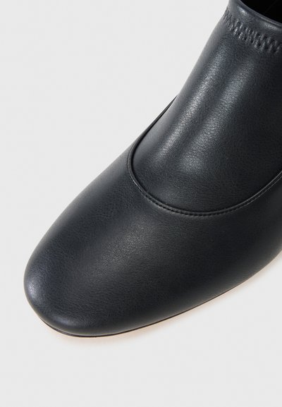 Pantofii din piele neagră au o textură netedă, vârful ascuțit și accente cusute aproape de gleznă. Designul este elegant și minimal.