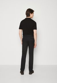 Polo negro de manga corta combinado con pantalones negros. La tela parece suave y ajustada, con un sutil detalle en los pantalones.