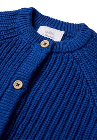 Cardigan blu lavorato a maglia con texture a coste, due bottoni in legno e scollatura rotonda. L'etichetta recita "Stellou & friends."