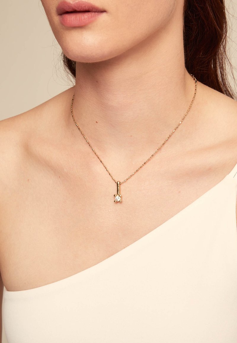 Collar de cadena de oro con un pequeño colgante de piedra preciosa transparente, que presenta un diseño geométrico simple y una textura suave y brillante.