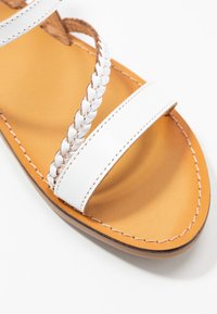 Witte sandalen met twee brede banden en een gevlochten accent. Gladde leren textuur met een tan inlegzool en contrasterende stikseldetails.