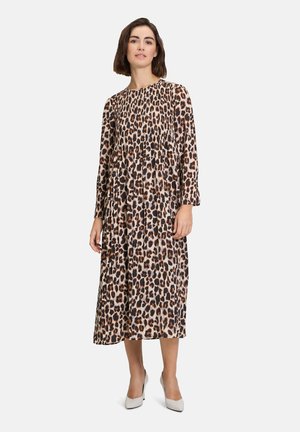 Robe à manches longues avec imprimé léopard, décolleté arrondi, taille froncée et jupe fluide, fabriquée en tissu léger, associée à des chaussures à talons blancs.