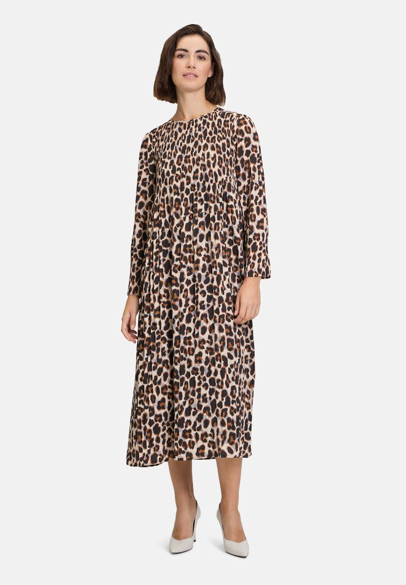 Šaty s dlouhým rukávem v leopardím vzoru, zaoblený výstřih, nabraný pas a splývavá sukně, vyrobené z lehkého materiálu, doplněné bílými podpatky.
