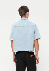 Lys blå denim kortærmet skjorte med frynser, krave og sømdetaljer, parret med sorte cargo-bukser med et orange mærke.