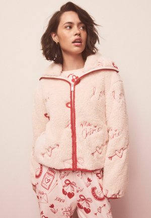 Mīksta rozā jaka ar sarkaniem akcentiem un sirds rakstiem, aprīkota ar rāvējslēdzēja aizdari un sānu kabatām, kombinēta ar rakstainām biksēm.