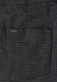 Gros plan d'une poche en tissu à carreaux gris foncé avec une petite étiquette métallique "Street One" dans le coin supérieur gauche de la poche.