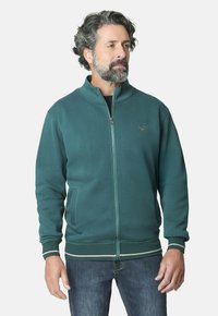 Chaqueta de cremallera en color verde azulado con un alto cuello, puños acanalados y dobladillo a rayas en contraste. Presenta bolsillos laterales y un sutil bordado de logo.