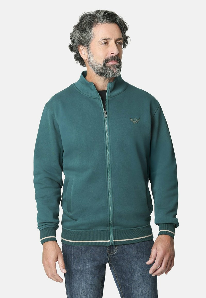 Chaqueta de cremallera en color verde azulado con un alto cuello, puños acanalados y dobladillo a rayas en contraste. Presenta bolsillos laterales y un sutil bordado de logo.