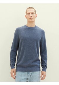 Niebieski sweter dziewiarski z okrągłym dekoltem, długimi rękawami i prążkowanymi mankietami. Charakteryzuje się fakturowanym materiałem oraz małym detalem logo na dole.