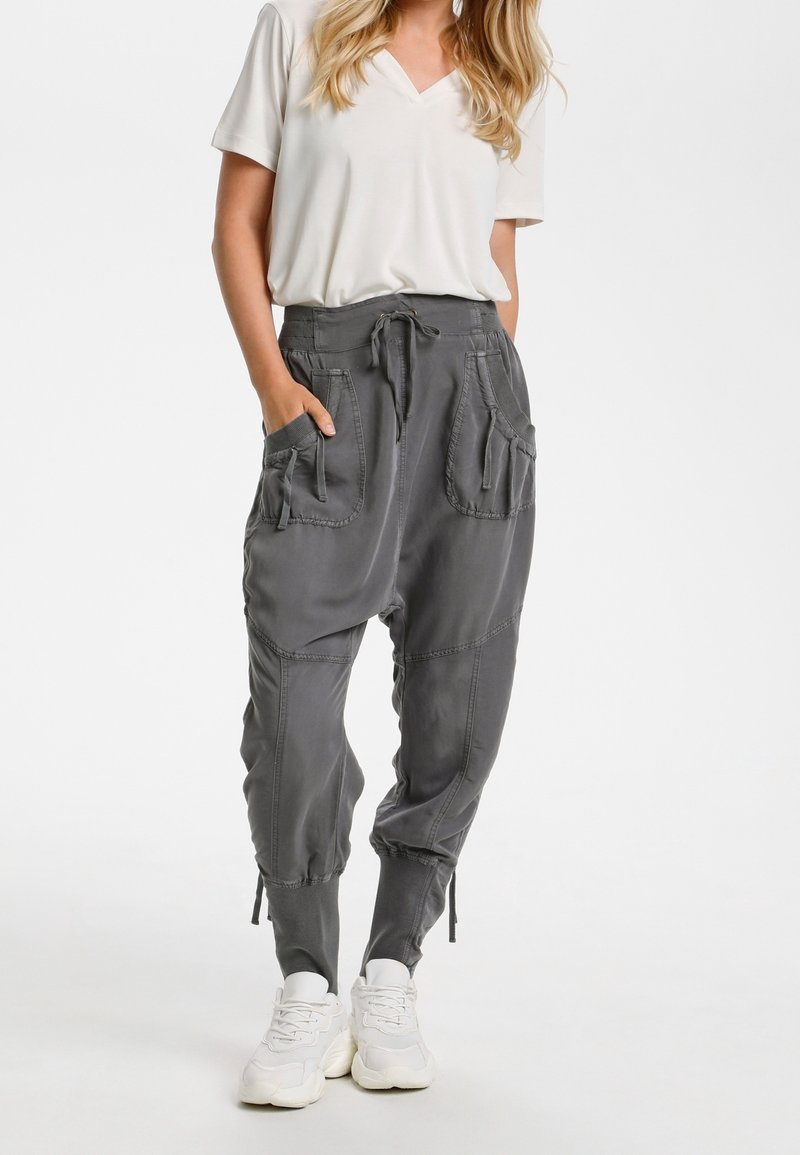 Grå cargobyxor med flera fickor, dragsko i midjan, avsmalnande anklar och mjukt material, kombinerat med en vit t-shirt med v-ringning och sneakers.