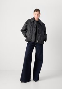 Zwarte, gequiltte jas met grote kraag en drukknoopsluitingen, gecombineerd met wijde denim jeans in een donkere kleur met een lichte flare aan de onderkant.