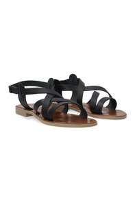 Schwarze Ledersandalen mit flachen Sohlen, ausgestattet mit überkreuzten Riemen und einem glatten braunen Fußbett. Verstellbarer Knöchelriemen zur Befestigung.