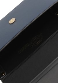 Portafoglio rettangolare in pelle blu navy con chiusura a pressione dorata. L'interno è foderato in nero e presenta dettagli con logo stampato. Texture liscia.