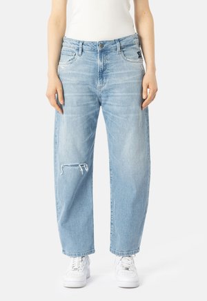 Lyseblå avslappet jeans med en liten rift på høyre kne, brukt med hvite joggesko og en hvit utenermet topp.