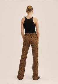 Pantalons marron avec un motif zèbre ondulé, présentant une coupe ample et une taille élastique, associés à un débardeur noir ajusté.