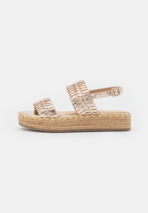 Sandales espadrilles métalliques dorées avec deux lanières tressées, fermeture à boucle à la cheville et semelle en jute tressé.