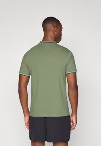 Olivenfarget polo-skjorte med kontrasterende stripete krage, korte ermer og sporty passform, iført med svarte shorts. Glatt tekstur.