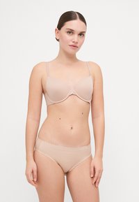 Nude-colored padded bra with adjustable straps, smooth texture, and scalloped edges; matching panties with a minimalist design and soft fabric.