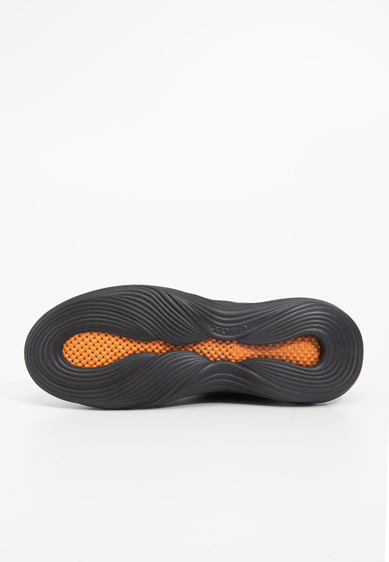 Semelle de chaussure noire avec des rainures ondulées et une section texturée orange comportant de petits trous pour la ventilation. Conçue pour le confort et le soutien.