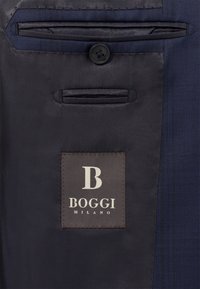 Interior de tela azul marino con un patrón de cuadros texturizado. Presenta un botón negro y una etiqueta marrón con letras blancas: "B BOGGI MILANO."