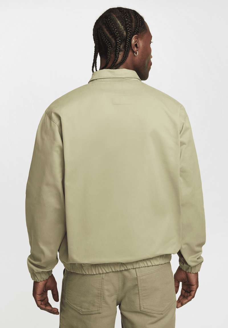 Veste en nylon beige clair avec un col arrondi, des poignets et un ourlet élastiques. Présente une texture lisse et un design uni sans motifs.