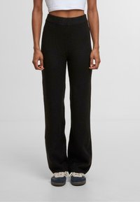 Kalhoty s vysokým pasem a širokým střihem v černé barvě, vyrobené z měkké, texturované tkaniny. Obsahují žebrovaný pas a uvolněný střih. Vhodné pro neformální nošení.