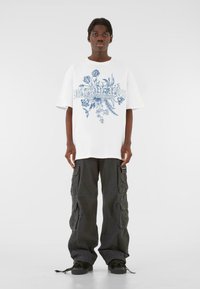 Hvid oversized t-shirt med blåt blomstermotiv, parret med løse sorte cargo-bukser med flere lommer og snore i bunden.