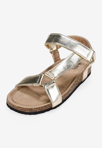 Sandales métalliques dorées avec de larges brides, semelle en liège et semelle texturée. Comprend des éléments réglables pour un maintien sécurisé.