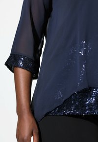 Marinebluse aus transparenter Stoff mit Dreiviertelärmeln. Saum verziert mit glänzenden marineblauen Pailletten. Weiche Textur mit lockerer Silhouette.